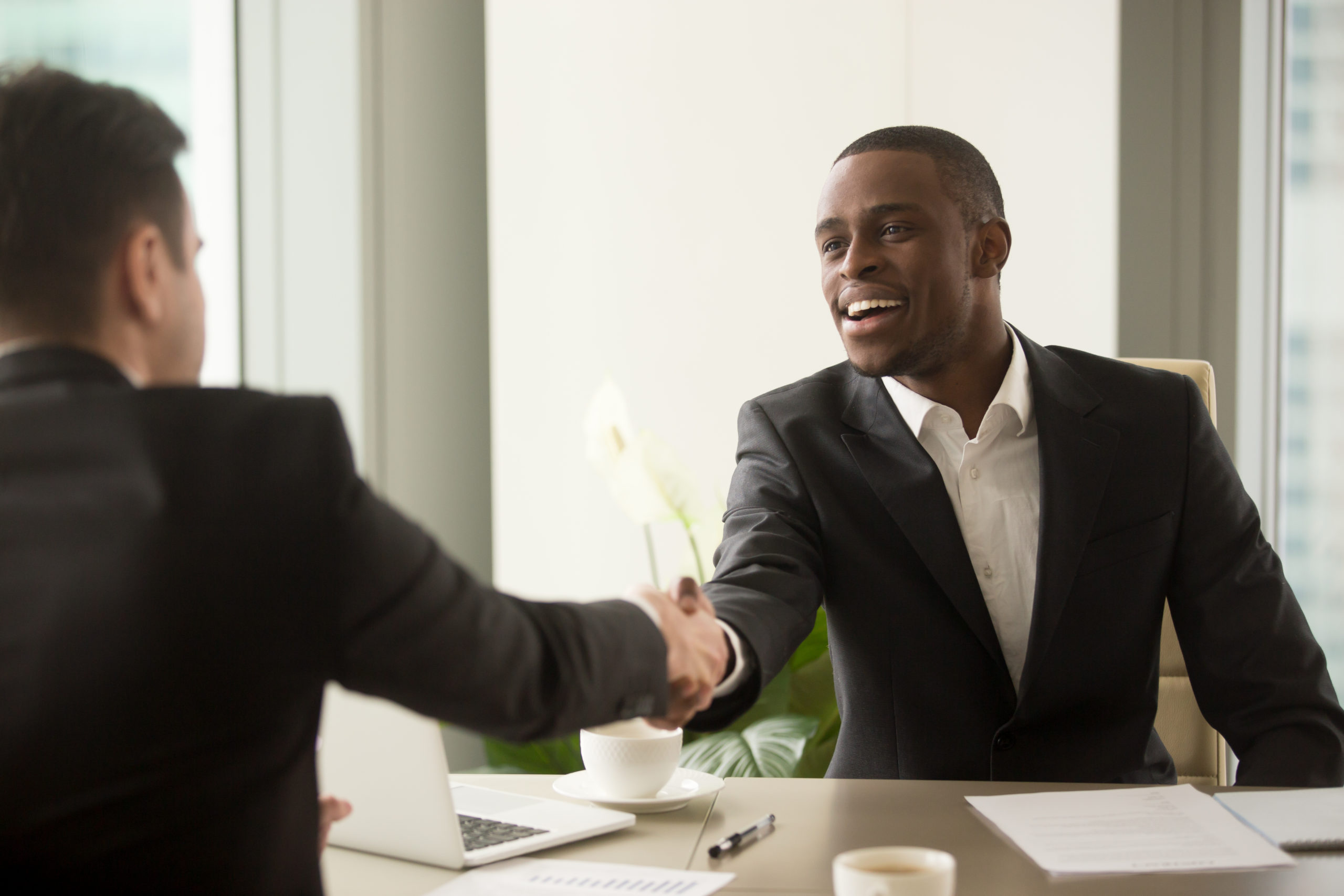 Two,Multicultural,Businessmen,Handshaking,Over,Desk,,Attractive,African,Entrepreneur,Shaking